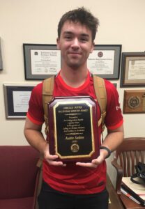 Austin Seekins hold his award while wearing a red shirt.