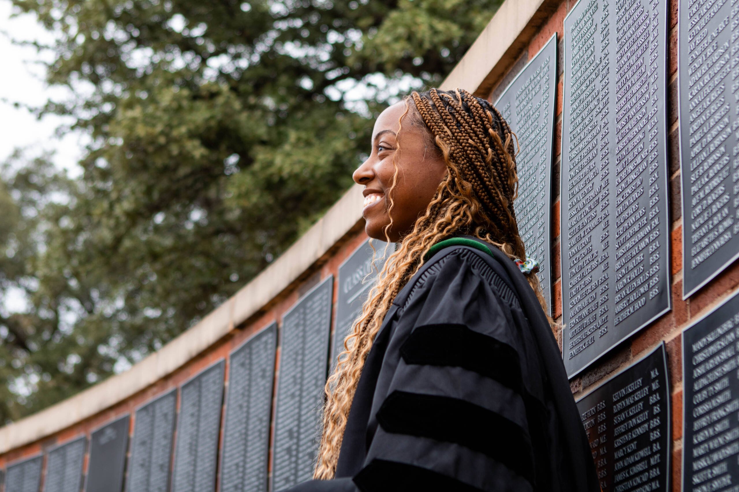 Doctoral Student talking in front of the alumni wall