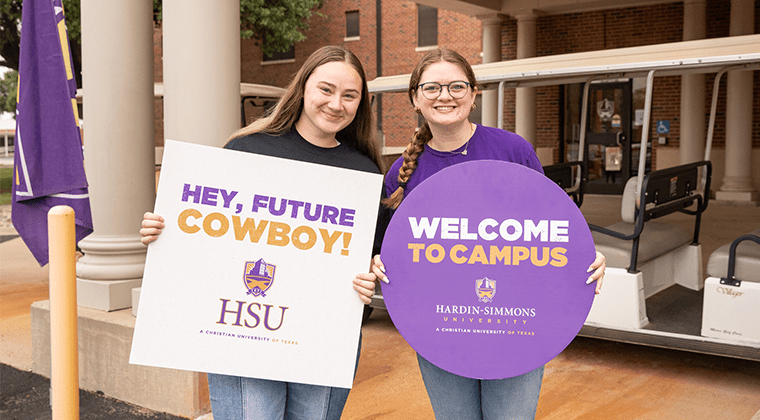 Two tour guides holding up signs to welcome new students.