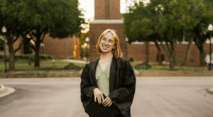 Courtney Govea posing in front of Hardin-Simmons University’s bell tower in her graduation gown.