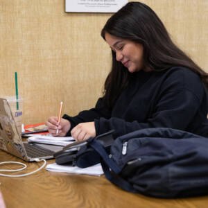 Female student studying in the library with her laptop and notes.